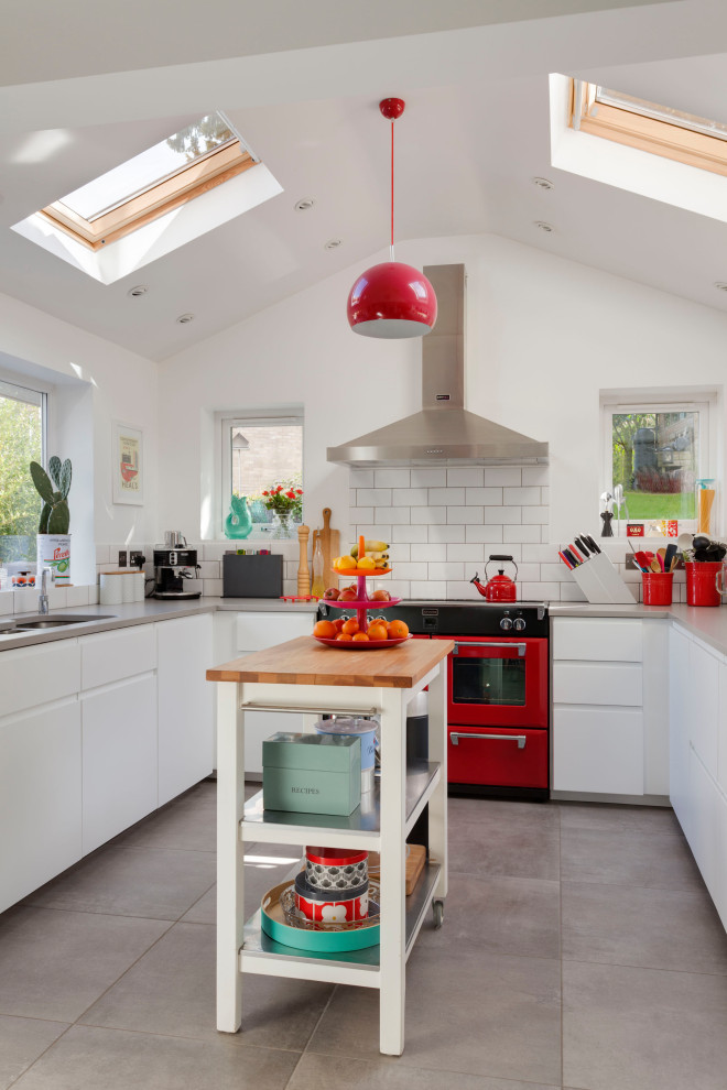 This is an example of a mid-sized eclectic u-shaped kitchen in Kent with an undermount sink, flat-panel cabinets, white cabinets, white splashback, subway tile splashback, stainless steel appliances, ceramic floors, with island, grey floor and grey benchtop.