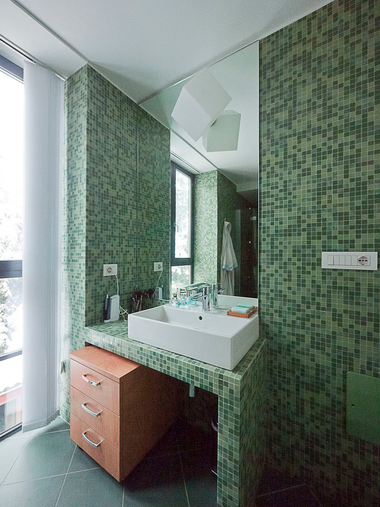 Small contemporary master bathroom in Milan with tile benchtops, an alcove shower, a two-piece toilet, green tile, mosaic tile, green walls, ceramic floors, flat-panel cabinets, light wood cabinets, a trough sink, green floor, a hinged shower door and green benchtops.