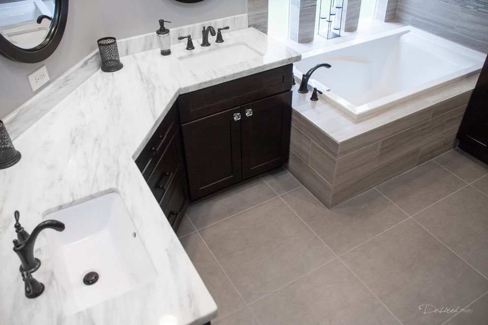 Photo of a large transitional master bathroom in Houston with an undermount sink, shaker cabinets, dark wood cabinets, quartzite benchtops, a drop-in tub, a corner shower, a two-piece toilet, gray tile, porcelain tile, grey walls and porcelain floors.
