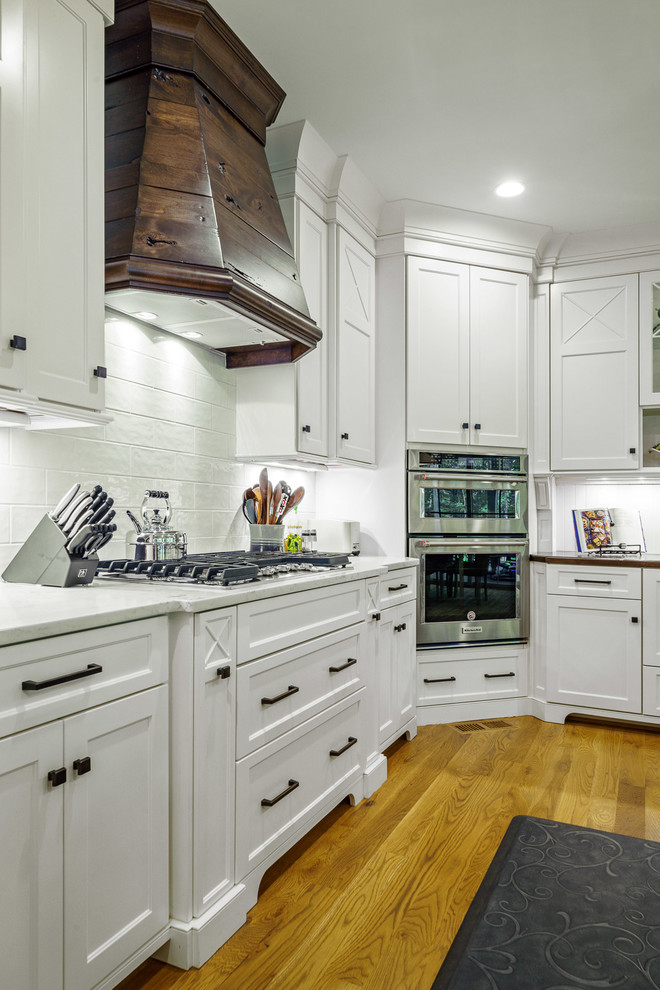 Eat-in kitchen - large transitional u-shaped medium tone wood floor and brown floor eat-in kitchen idea with a farmhouse sink, recessed-panel cabinets, white cabinets, quartz countertops, white backsplash, ceramic backsplash, stainless steel appliances, an island and white countertops