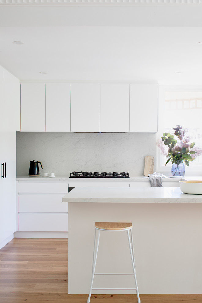 Photo of a mid-sized contemporary u-shaped eat-in kitchen in Melbourne with an undermount sink, flat-panel cabinets, white cabinets, quartz benchtops, engineered quartz splashback, black appliances, medium hardwood floors, no island and brown floor.