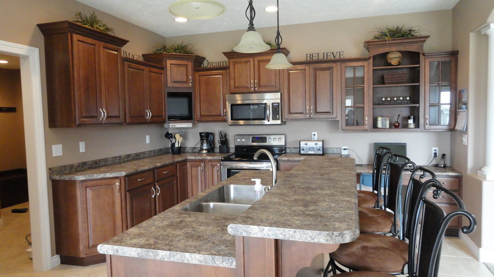 Example of a mid-sized l-shaped open concept kitchen design with an undermount sink, raised-panel cabinets, dark wood cabinets, laminate countertops, stainless steel appliances, beige walls and an island