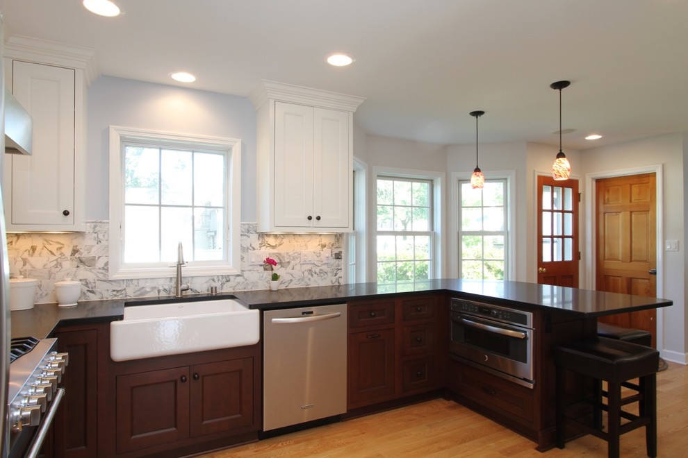 Photo of a large transitional u-shaped eat-in kitchen in Milwaukee with shaker cabinets, white cabinets, white splashback, marble splashback, stainless steel appliances, light hardwood floors, a peninsula, a farmhouse sink and granite benchtops.