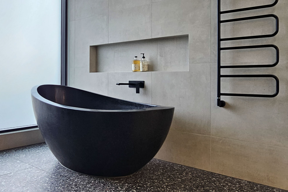 Design ideas for an expansive contemporary ensuite bathroom in Melbourne with black cabinets, a freestanding bath, beige tiles, porcelain flooring, solid surface worktops, black floors, an enclosed toilet, double sinks and a floating vanity unit.
