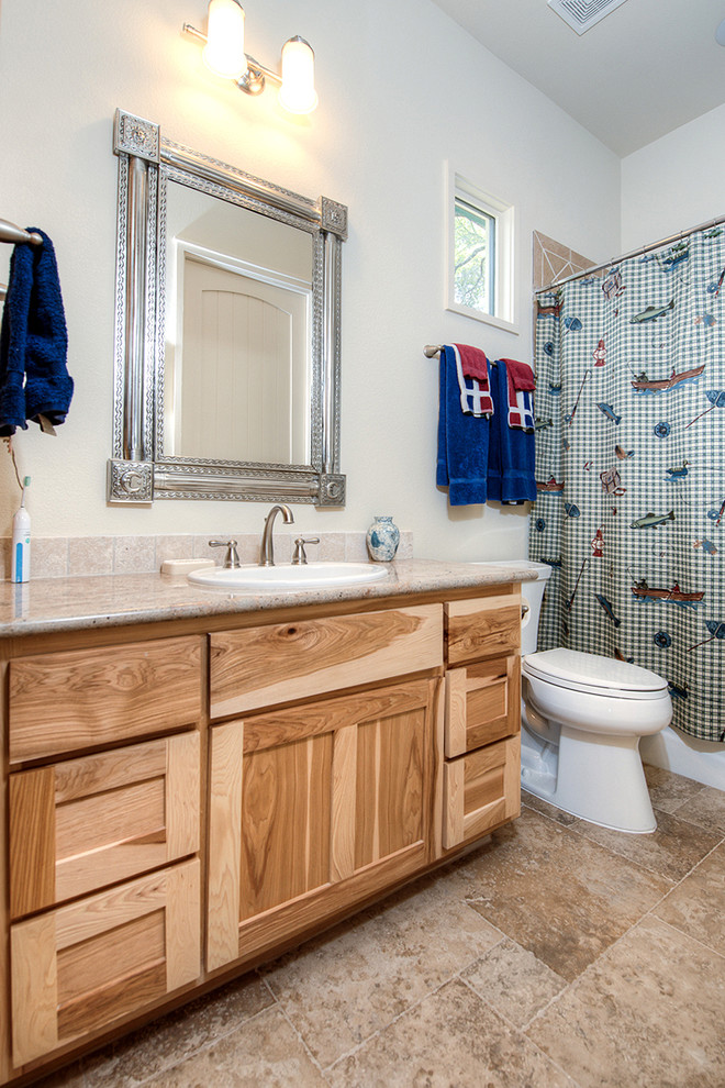 Design ideas for a mid-sized country 3/4 bathroom in Austin with shaker cabinets, light wood cabinets, an alcove tub, a shower/bathtub combo, a two-piece toilet, white walls, travertine floors, a drop-in sink, granite benchtops, brown floor, a shower curtain and beige benchtops.