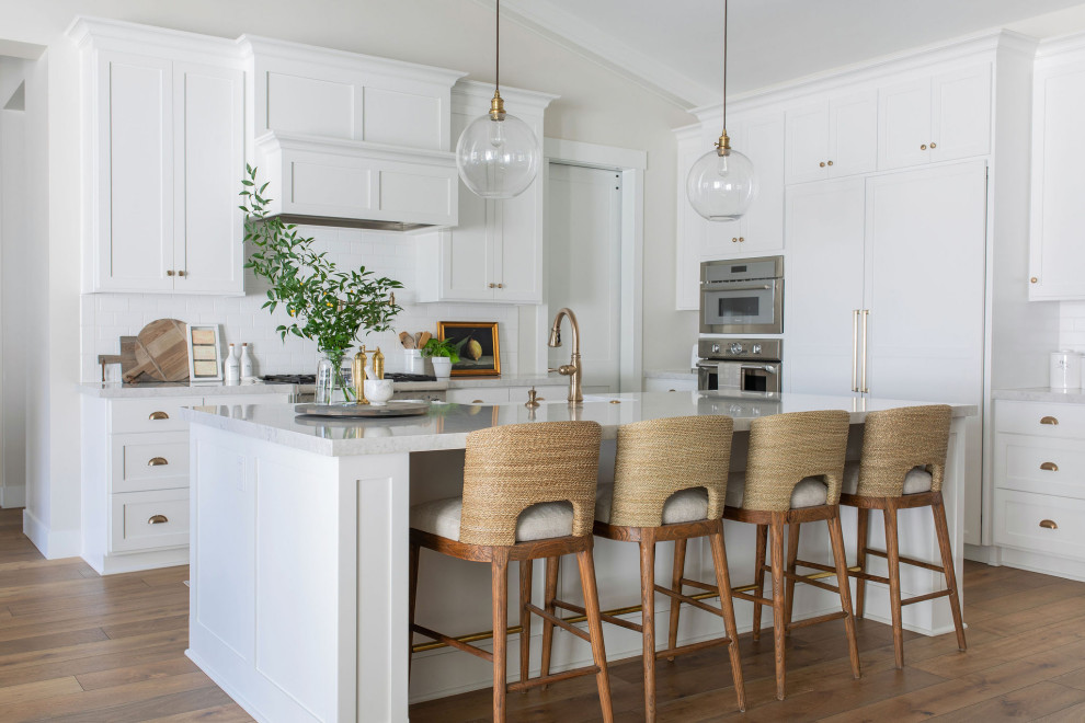 Design ideas for a large transitional l-shaped open plan kitchen in Sacramento with a farmhouse sink, shaker cabinets, white cabinets, quartz benchtops, white splashback, ceramic splashback, stainless steel appliances, medium hardwood floors, with island, brown floor, grey benchtop and vaulted.