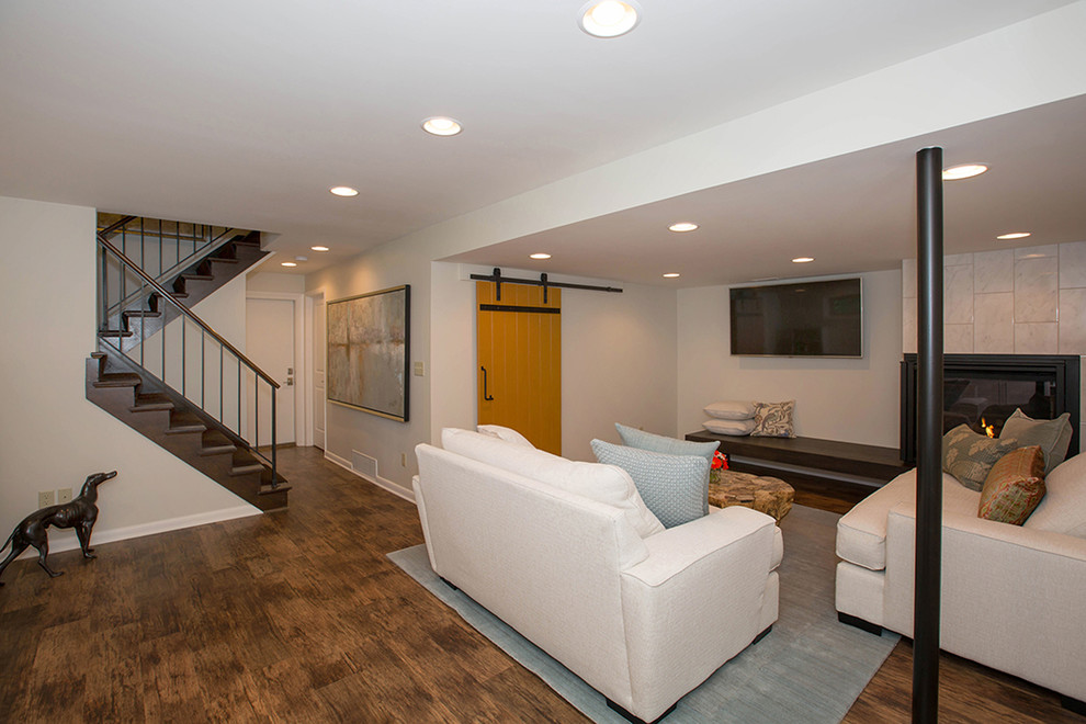 Mid-sized contemporary fully buried basement in Cincinnati with beige walls, medium hardwood floors, a corner fireplace, a tile fireplace surround and brown floor.