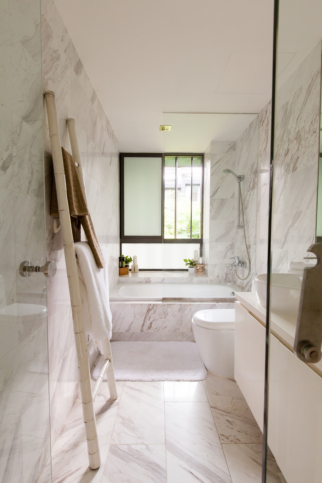 This is an example of a contemporary bathroom in Singapore with a vessel sink, flat-panel cabinets, white cabinets, an alcove tub, a shower/bathtub combo, a one-piece toilet, white tile, white walls and marble floors.