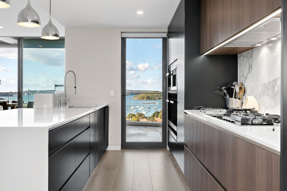 Photo of a large contemporary galley open plan kitchen in Sydney with an integrated sink, black cabinets, quartz benchtops, grey splashback, marble splashback, stainless steel appliances, medium hardwood floors, with island, brown floor and white benchtop.