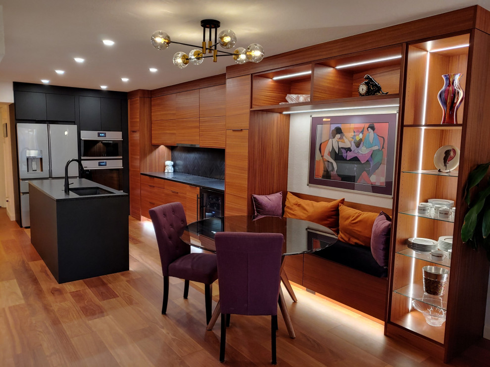 Inspiration for a mid-sized midcentury l-shaped eat-in kitchen in Tampa with a single-bowl sink, flat-panel cabinets, medium wood cabinets, granite benchtops, black splashback, ceramic splashback, stainless steel appliances, medium hardwood floors, with island and black benchtop.