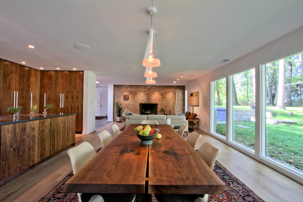 Design ideas for a mid-sized midcentury open plan dining in Indianapolis with white walls, light hardwood floors, a standard fireplace, a brick fireplace surround and beige floor.