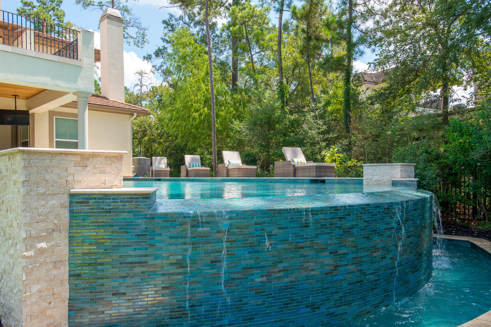 This is an example of a large transitional backyard rectangular infinity pool in Houston with a hot tub and natural stone pavers.
