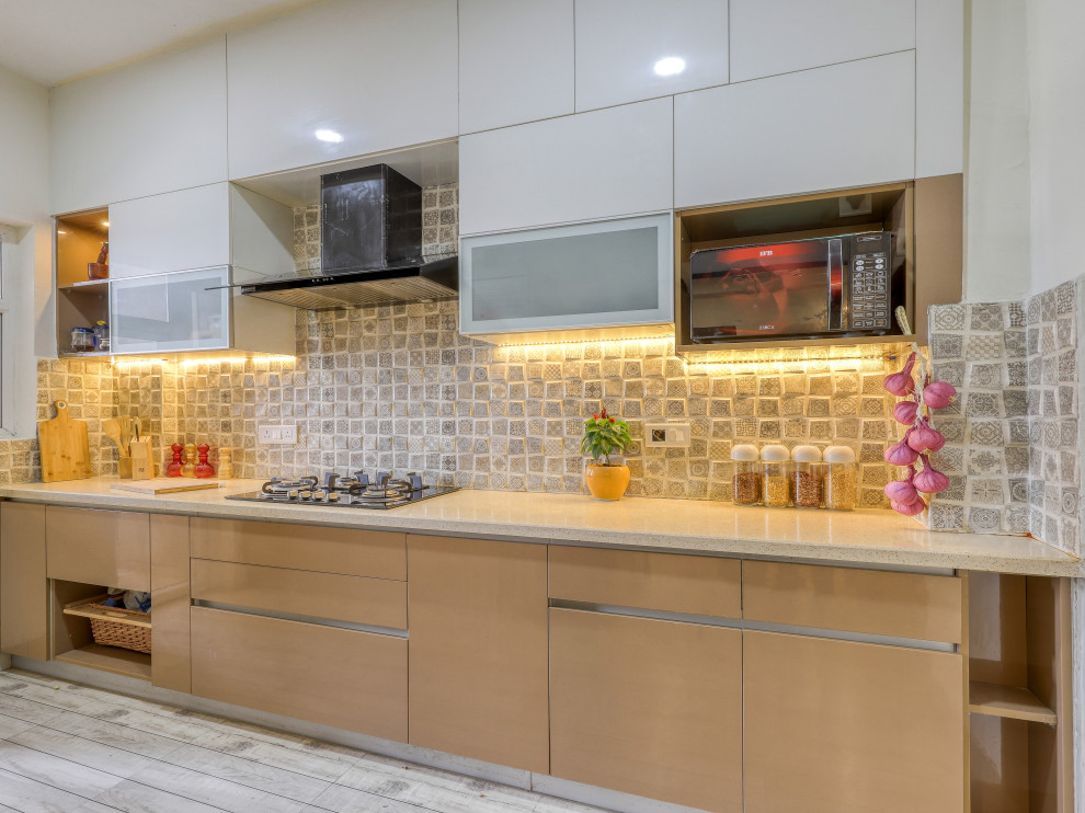 Photo of a mid-sized mediterranean galley kitchen in Bengaluru with flat-panel cabinets, beige cabinets, grey splashback, panelled appliances, no island, grey floor and beige benchtop.