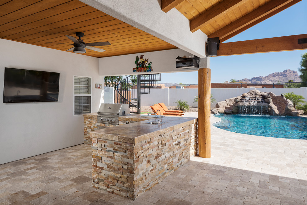 This is an example of a large tropical backyard patio in Phoenix with an outdoor kitchen, concrete pavers and a pergola.