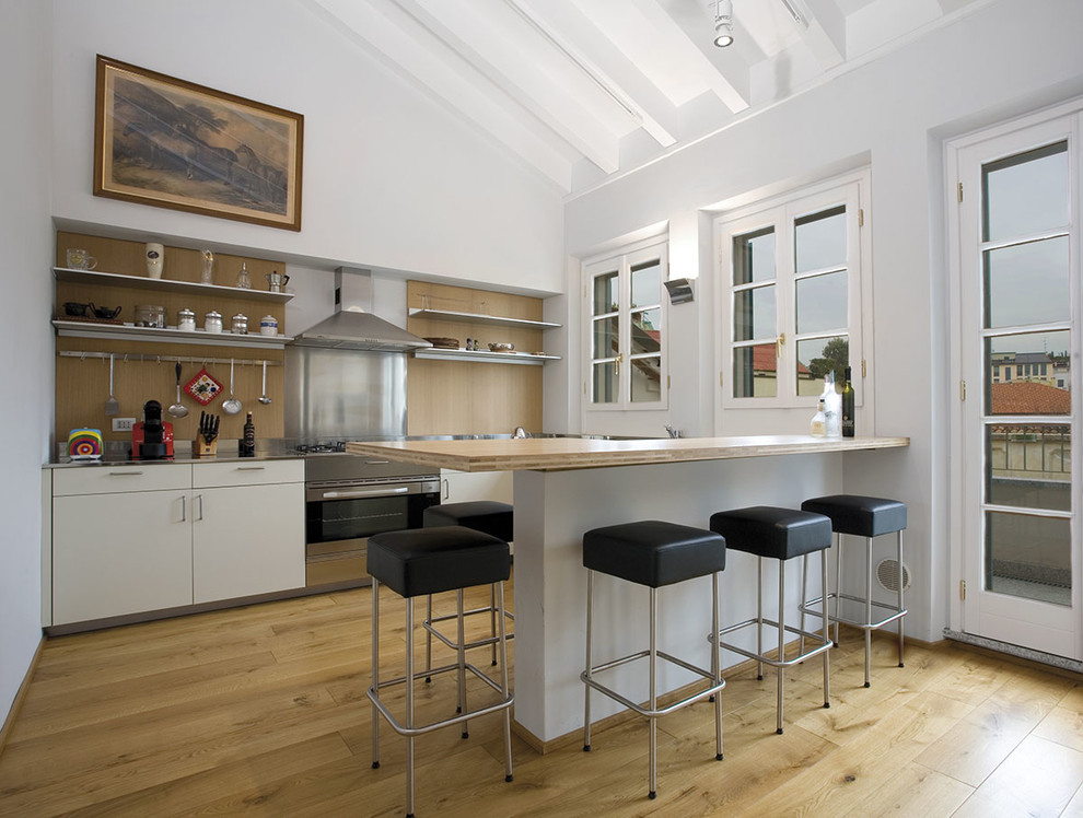 Photo of a mid-sized modern single-wall eat-in kitchen in Milan with stainless steel appliances, light hardwood floors, flat-panel cabinets, white cabinets, stainless steel benchtops, metallic splashback, a peninsula, a double-bowl sink and exposed beam.