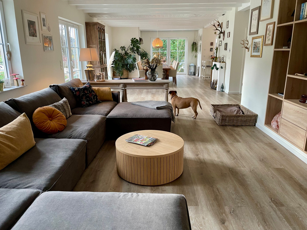 Design ideas for a large farmhouse grey and white open plan living room in Cologne with beige walls, vinyl flooring, a wall mounted tv, brown floors and exposed beams.