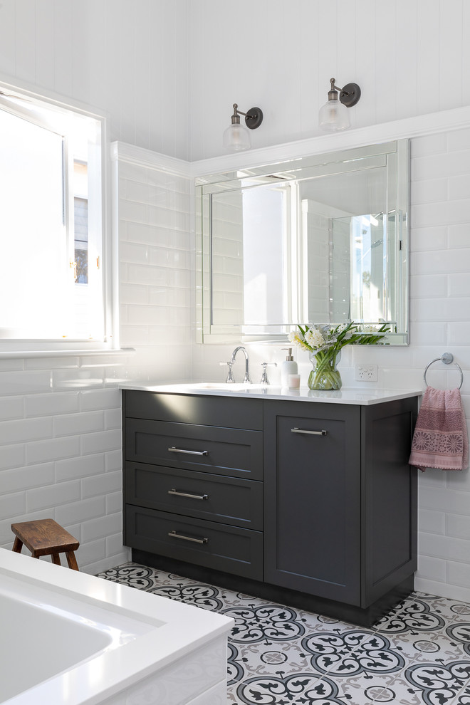 This is an example of a traditional bathroom in Brisbane with shaker cabinets, black cabinets, a drop-in tub, a shower/bathtub combo, white tile, white walls, an undermount sink, engineered quartz benchtops and white benchtops.