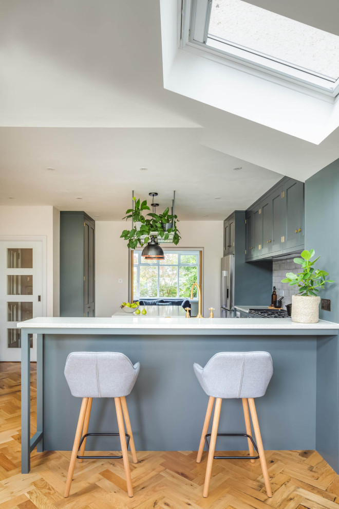 This is an example of a large contemporary l-shaped open plan kitchen in London with shaker cabinets, grey cabinets, an island and white worktops.