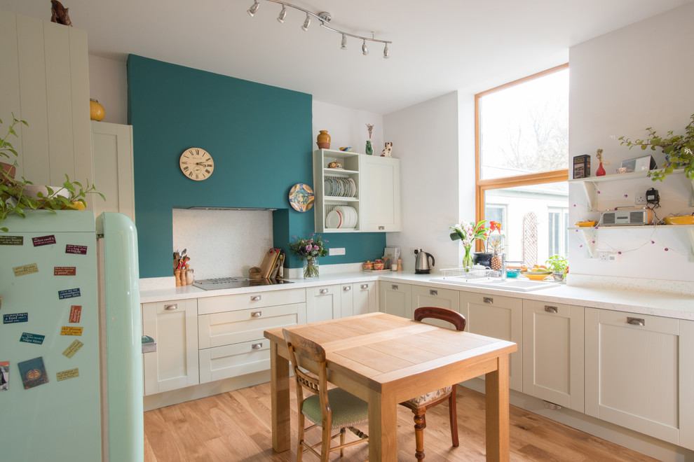 Inspiration for a mid-sized contemporary u-shaped eat-in kitchen in Other with a double-bowl sink, shaker cabinets, green cabinets, solid surface benchtops, white splashback, panelled appliances, light hardwood floors and no island.