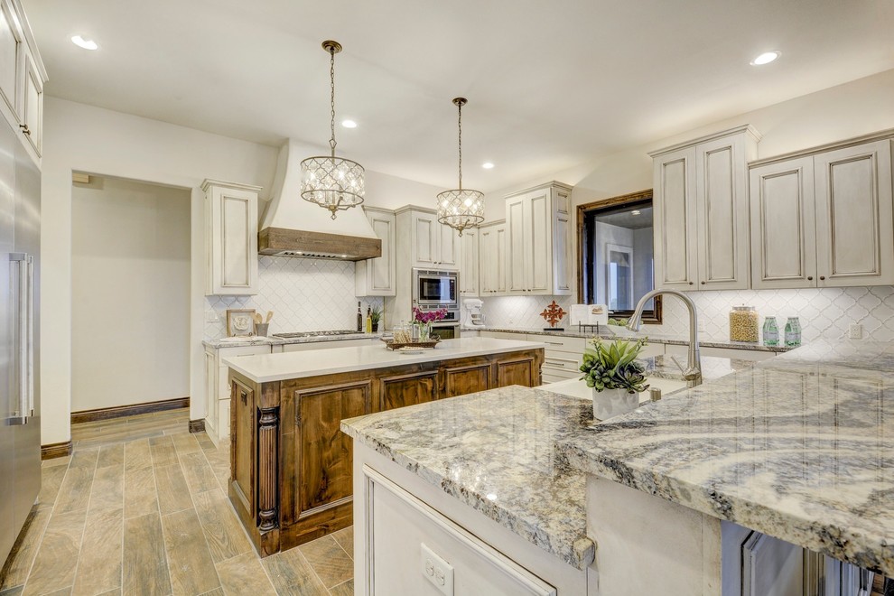 Inspiration for a large transitional u-shaped eat-in kitchen in Austin with an undermount sink, recessed-panel cabinets, distressed cabinets, granite benchtops, white splashback, ceramic splashback, stainless steel appliances, porcelain floors, multiple islands and brown floor.