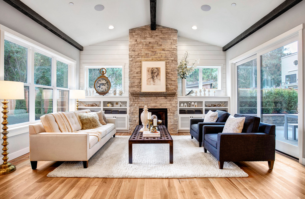 Inspiration for a transitional open concept living room in Seattle with light hardwood floors, a standard fireplace, a stone fireplace surround, a wall-mounted tv and beige walls.
