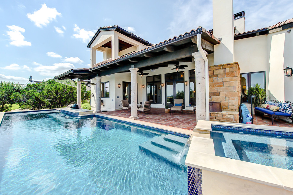 This is an example of a large country backyard rectangular infinity pool in Austin with tile.