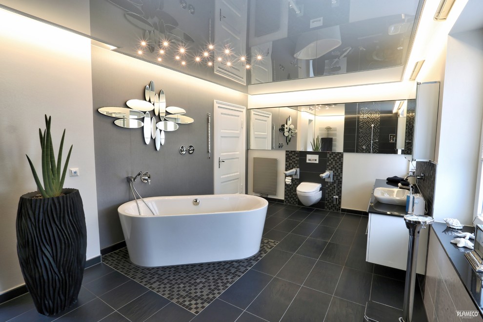 Großes Modernes Duschbad mit weißen Schränken, freistehender Badewanne, Wandtoilette mit Spülkasten, grauen Fliesen, grauer Wandfarbe und Einbauwaschbecken in Sonstige