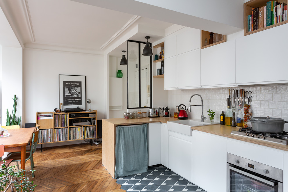 Small scandinavian l-shaped eat-in kitchen in Paris with a farmhouse sink, flat-panel cabinets, white cabinets, wood benchtops, white splashback, ceramic splashback, stainless steel appliances, cement tiles, no island, grey floor and beige benchtop.