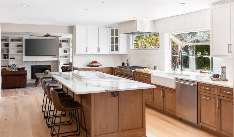 Inspiration for a large transitional light wood floor and brown floor open concept kitchen remodel in Seattle with a farmhouse sink, medium tone wood cabinets, quartz countertops, white backsplash, mosaic tile backsplash, stainless steel appliances, an island and white countertops