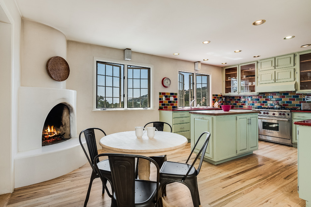 This is an example of a mid-sized u-shaped eat-in kitchen in Other with a double-bowl sink, shaker cabinets, green cabinets, multi-coloured splashback, subway tile splashback, stainless steel appliances, light hardwood floors, with island and beige floor.