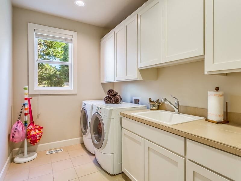Mid-sized traditional galley utility room in Seattle with a drop-in sink, recessed-panel cabinets, white cabinets, tile benchtops, beige walls, ceramic floors and a side-by-side washer and dryer.