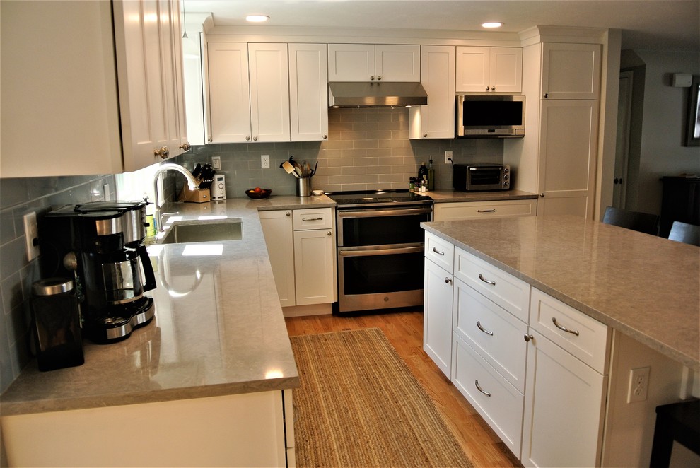 Kitchen - transitional light wood floor kitchen idea in Boston with an undermount sink, shaker cabinets, white cabinets, quartz countertops, gray backsplash, subway tile backsplash, stainless steel appliances, an island and gray countertops