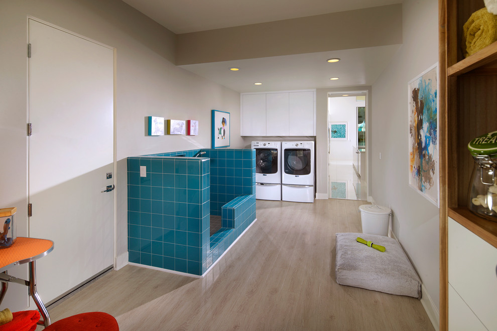 Inspiration for a midcentury utility room in Los Angeles with flat-panel cabinets, white cabinets, grey walls, light hardwood floors and a side-by-side washer and dryer.