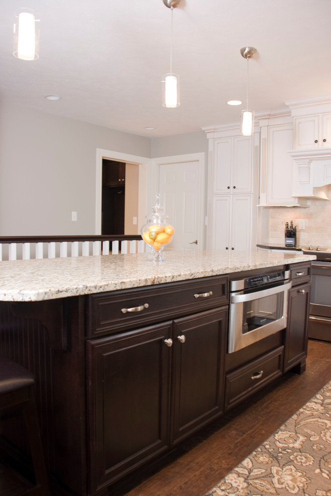 Example of a large transitional u-shaped medium tone wood floor kitchen design in Cincinnati with an undermount sink, recessed-panel cabinets, white cabinets, granite countertops, beige backsplash, stone tile backsplash, stainless steel appliances and an island