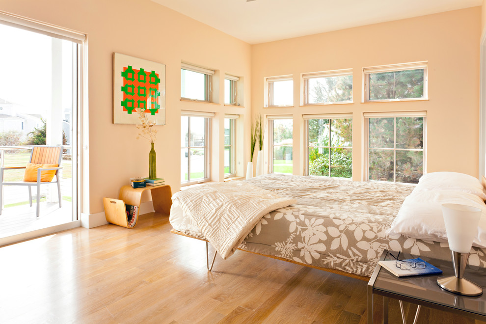 This is an example of a modern bedroom in Boston with beige walls and light hardwood floors.