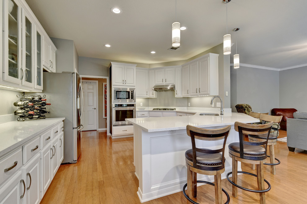 Eat-in kitchen - mid-sized transitional u-shaped light wood floor eat-in kitchen idea in Austin with an undermount sink, white cabinets, quartz countertops, white backsplash, stone slab backsplash, stainless steel appliances, a peninsula and raised-panel cabinets