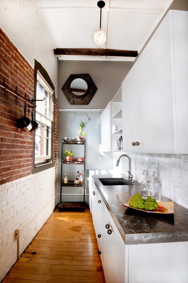 Photo of an industrial separate kitchen in Portland Maine with an undermount sink, flat-panel cabinets, white cabinets, white splashback and subway tile splashback.