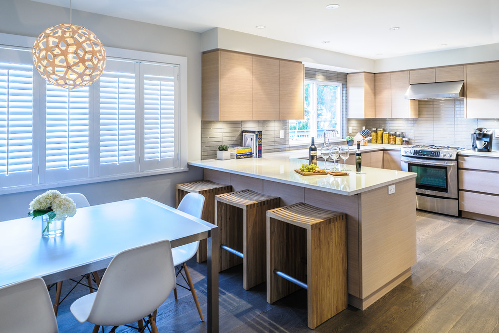 Mid-sized contemporary u-shaped eat-in kitchen in Vancouver with flat-panel cabinets, light wood cabinets, white splashback, stainless steel appliances, quartzite benchtops, glass tile splashback, light hardwood floors, with island and a double-bowl sink.