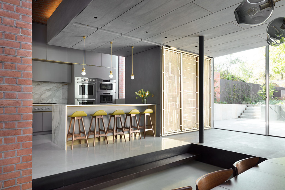Photo of a large contemporary l-shaped open plan kitchen in London with a submerged sink, flat-panel cabinets, grey cabinets, marble worktops, white splashback, marble splashback, stainless steel appliances, concrete flooring, an island, grey floors and white worktops.