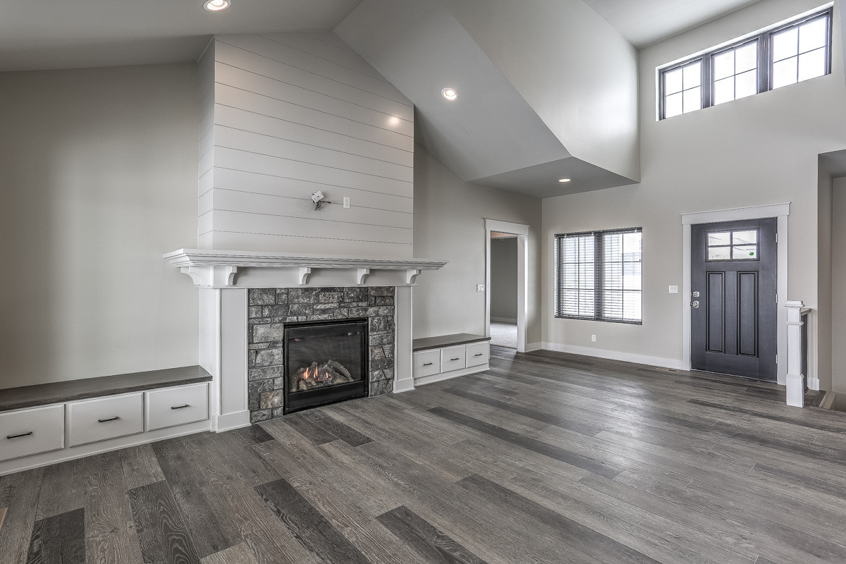 Example of a farmhouse open concept vinyl floor and gray floor family room design in Omaha with gray walls, a standard fireplace, a stone fireplace and a wall-mounted tv