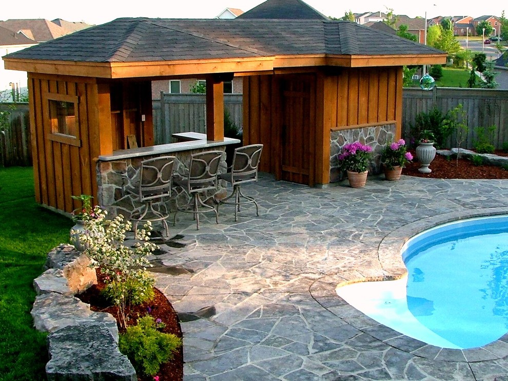 This is an example of a large traditional backyard kidney-shaped pool in Toronto with a pool house and natural stone pavers.