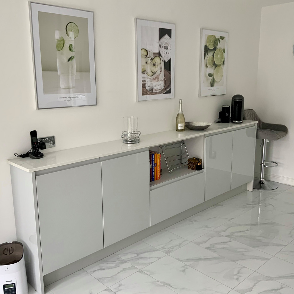Design ideas for a large contemporary grey and white u-shaped kitchen/diner in Buckinghamshire with flat-panel cabinets, grey cabinets, quartz worktops, grey splashback, glass sheet splashback, black appliances, a breakfast bar and white worktops.
