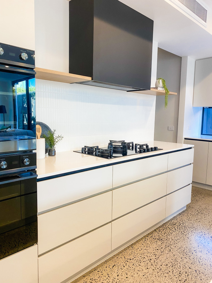 This is an example of a large contemporary l-shaped open plan kitchen in Melbourne with a double-bowl sink, beaded inset cabinets, grey cabinets, quartz benchtops, white splashback, ceramic splashback, black appliances, concrete floors, with island, grey floor and white benchtop.