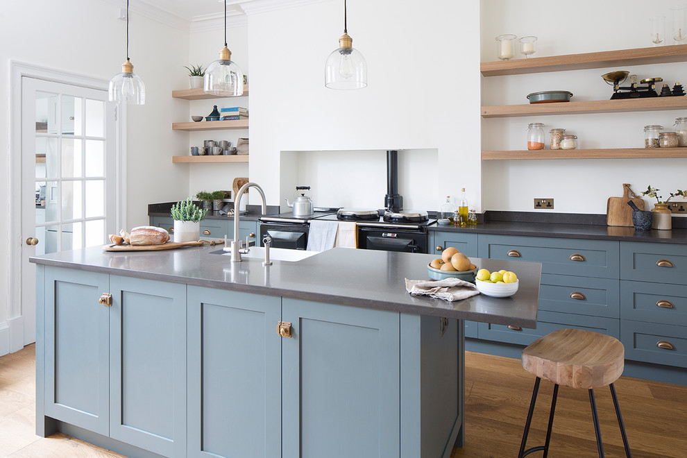 Photo of a mid-sized transitional single-wall eat-in kitchen in Edinburgh with a farmhouse sink, shaker cabinets, blue cabinets, quartz benchtops, black appliances, with island, white splashback and medium hardwood floors.