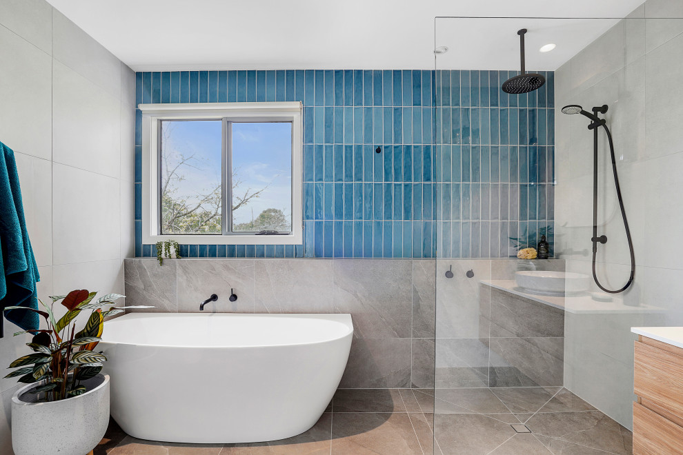 This is an example of a medium sized contemporary ensuite bathroom in Melbourne with flat-panel cabinets, light wood cabinets, a hot tub, a built-in shower, blue tiles, ceramic tiles, blue walls, porcelain flooring, engineered stone worktops, grey floors, an open shower, white worktops, a single sink and a floating vanity unit.