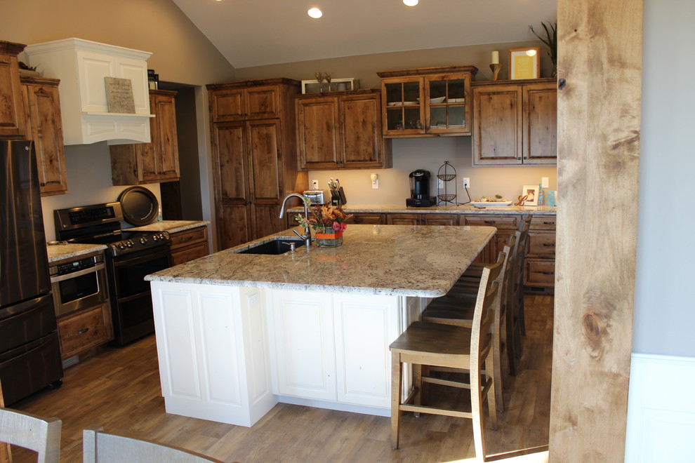 Example of a large mountain style l-shaped medium tone wood floor and brown floor open concept kitchen design with an undermount sink, raised-panel cabinets, medium tone wood cabinets, granite countertops, stainless steel appliances and an island