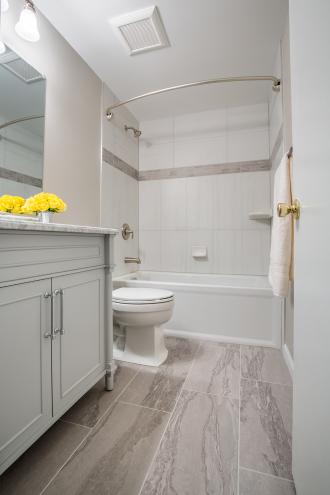 Photo of a small transitional kids bathroom in DC Metro with furniture-like cabinets, grey cabinets, an alcove tub, a shower/bathtub combo, a one-piece toilet, gray tile, beige walls, porcelain floors, an undermount sink, engineered quartz benchtops and porcelain tile.