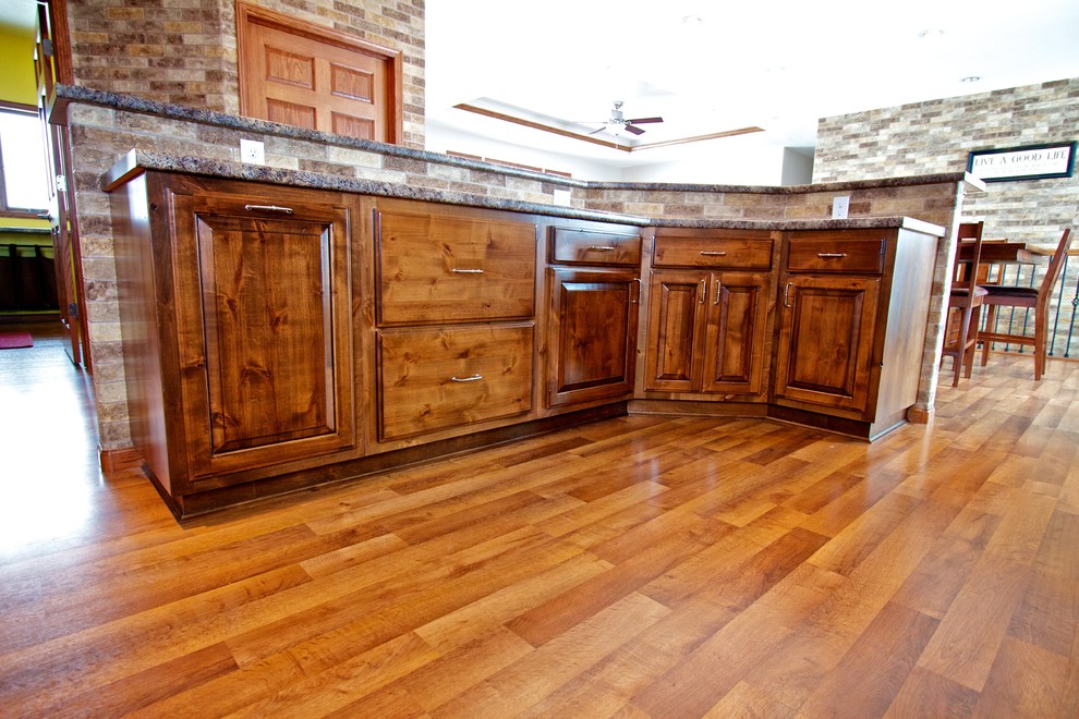 Inspiration for a mid-sized l-shaped medium tone wood floor open concept kitchen remodel with a drop-in sink, dark wood cabinets, laminate countertops, black appliances, an island and raised-panel cabinets