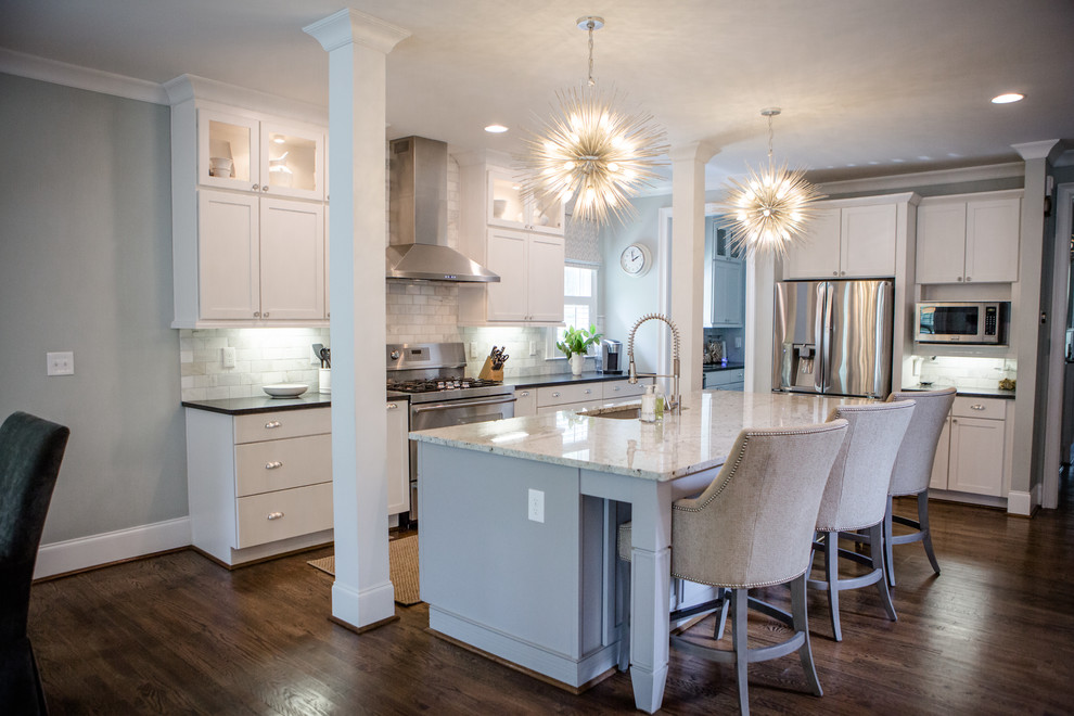 Large transitional l-shaped open plan kitchen in Atlanta with an undermount sink, shaker cabinets, white cabinets, quartz benchtops, multi-coloured splashback, marble splashback, stainless steel appliances, medium hardwood floors, with island, brown floor and black benchtop.