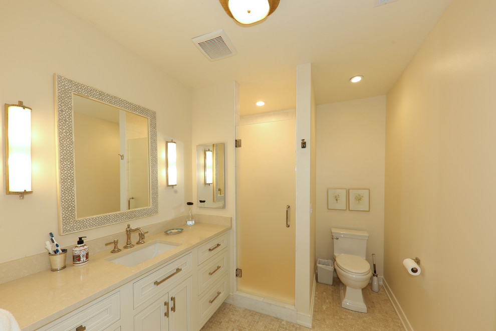 Design ideas for a beach style master bathroom in Milwaukee with beaded inset cabinets, white cabinets, an alcove shower, a two-piece toilet, white walls, mosaic tile floors, an undermount sink, marble benchtops, beige floor, a hinged shower door and beige benchtops.
